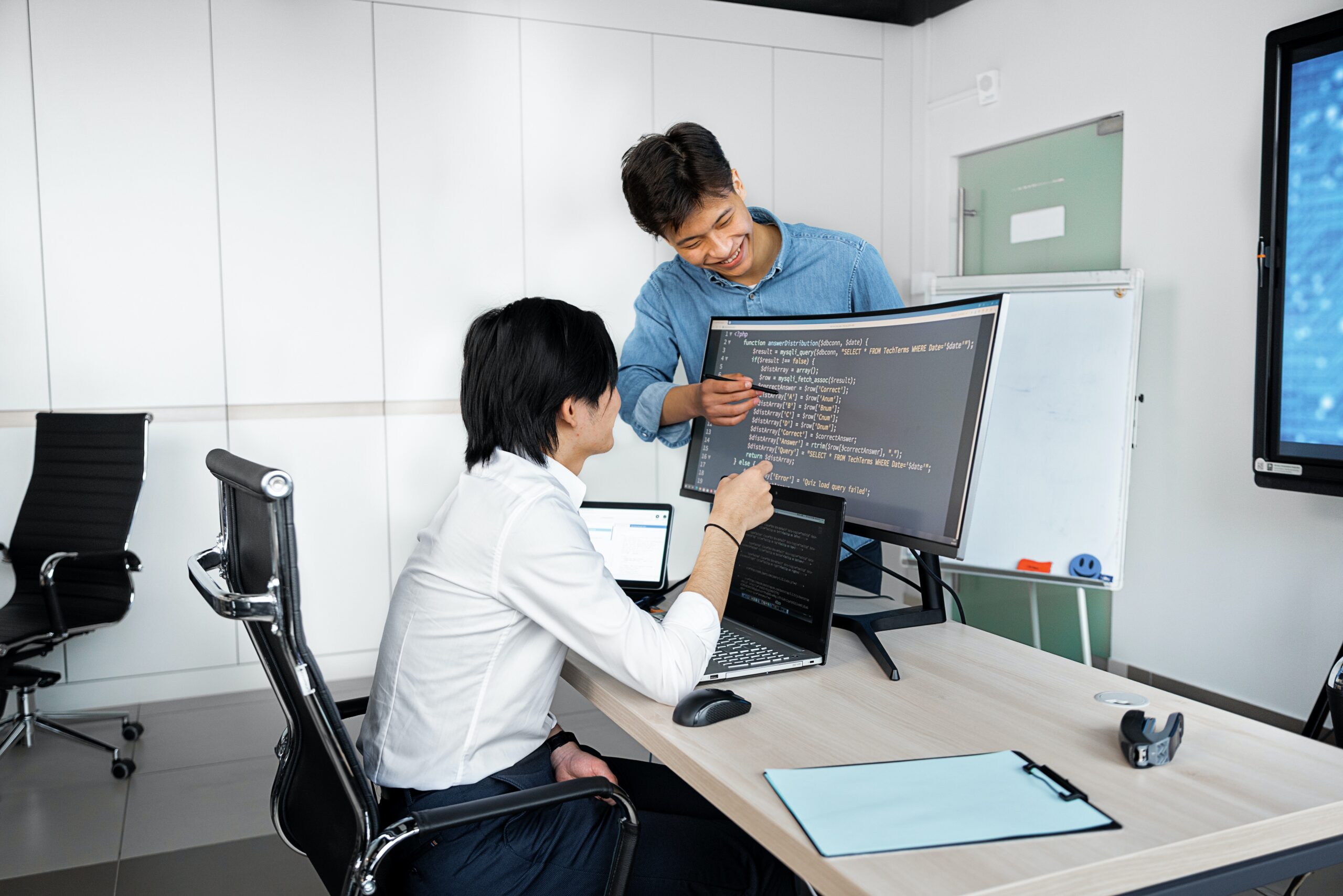 A software developer is discussing code with a colleague while writing code on a PC in suspenx office.